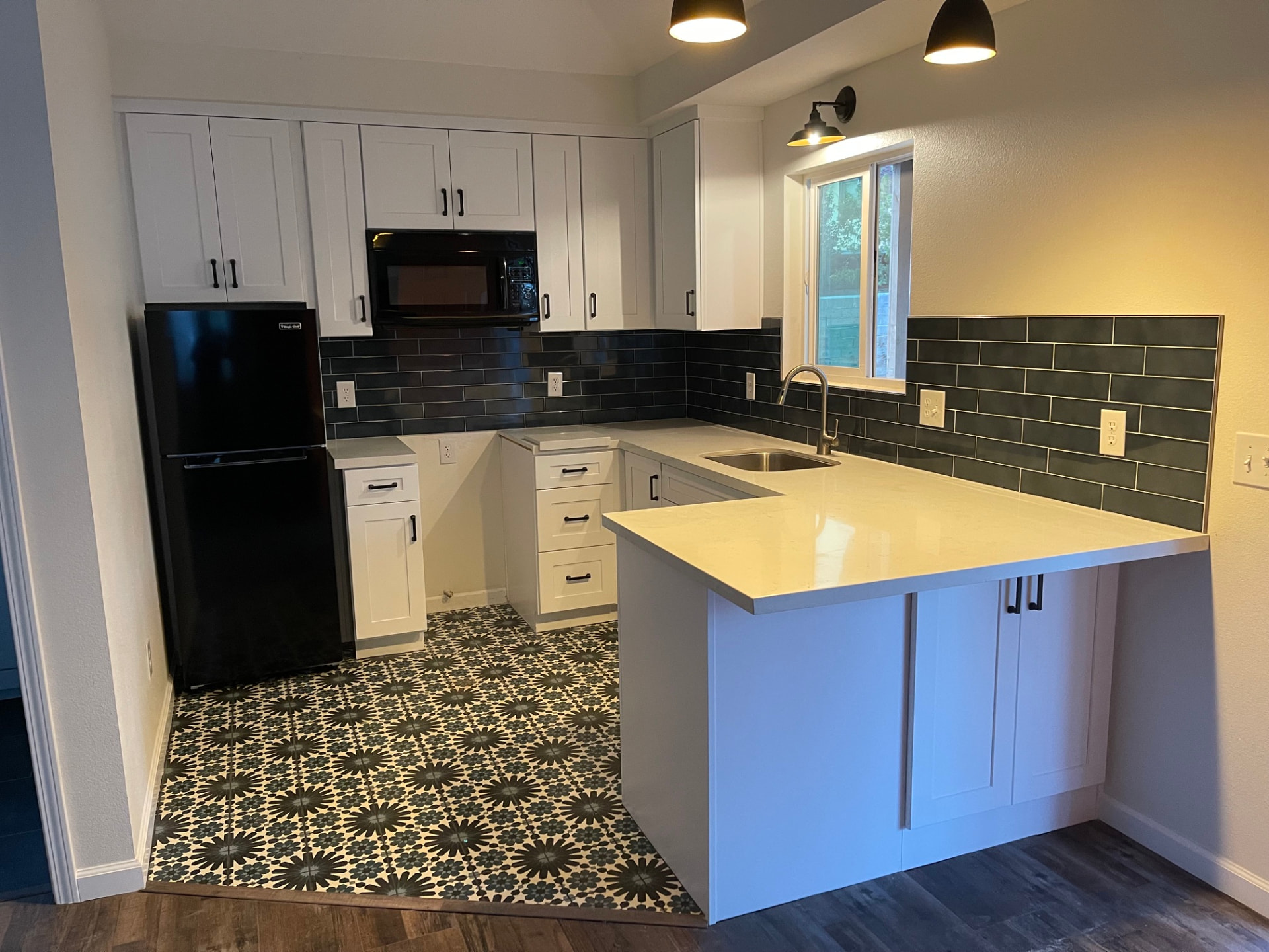 White shaker kitchen with dark subway backsplash and patterned tile floor