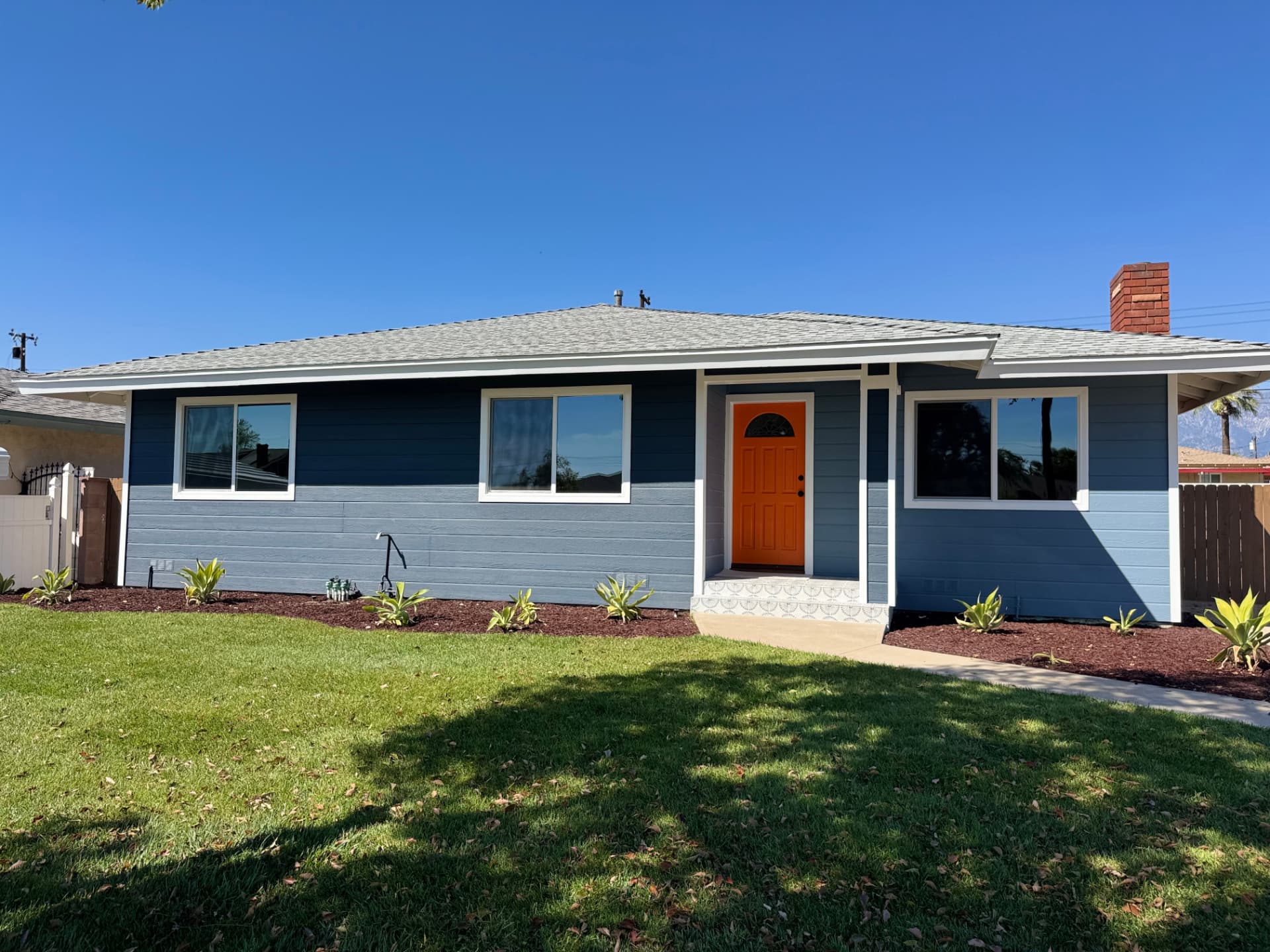Single-story home with new blue siding, windows and orange front door